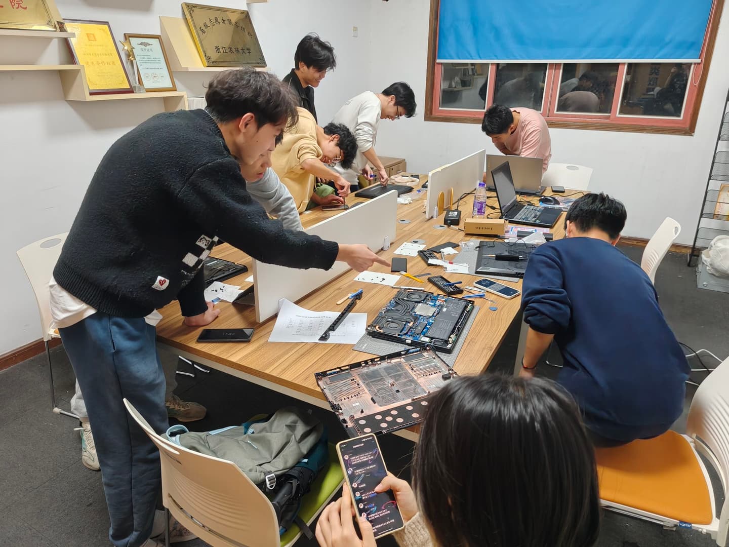 电脑医院成员围在桌边讨论一块拆下来的笔记本主板